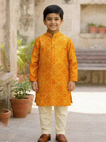 Young boy wearing an orange embroidered kurta with white pants standing outdoors.
