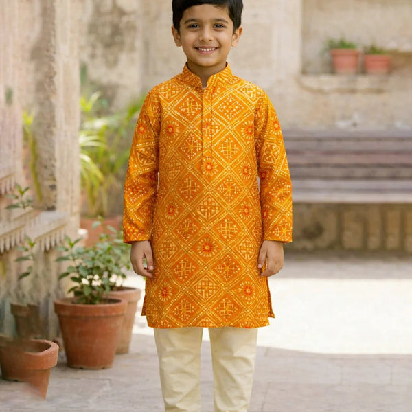 Young boy wearing an orange embroidered kurta with white pants standing outdoors.