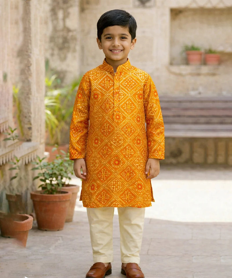 Young boy wearing an orange embroidered kurta with white pants standing outdoors.