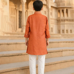 Person wearing an orange kurta with white pants standing on steps in front of a historic building.