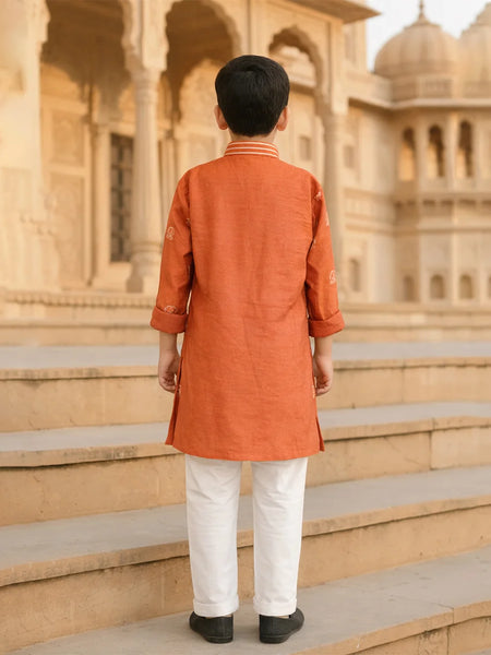 Person wearing an orange kurta with white pants standing on steps in front of a historic building.