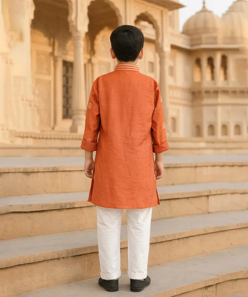 Person wearing an orange kurta with white pants standing on steps in front of a historic building.