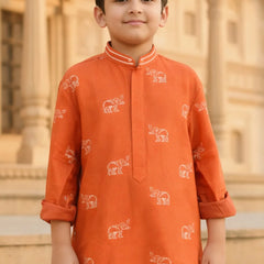 Child wearing an orange kurta with elephant patterns in front of a building.