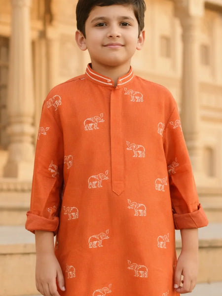 Child wearing an orange kurta with elephant patterns in front of a building.