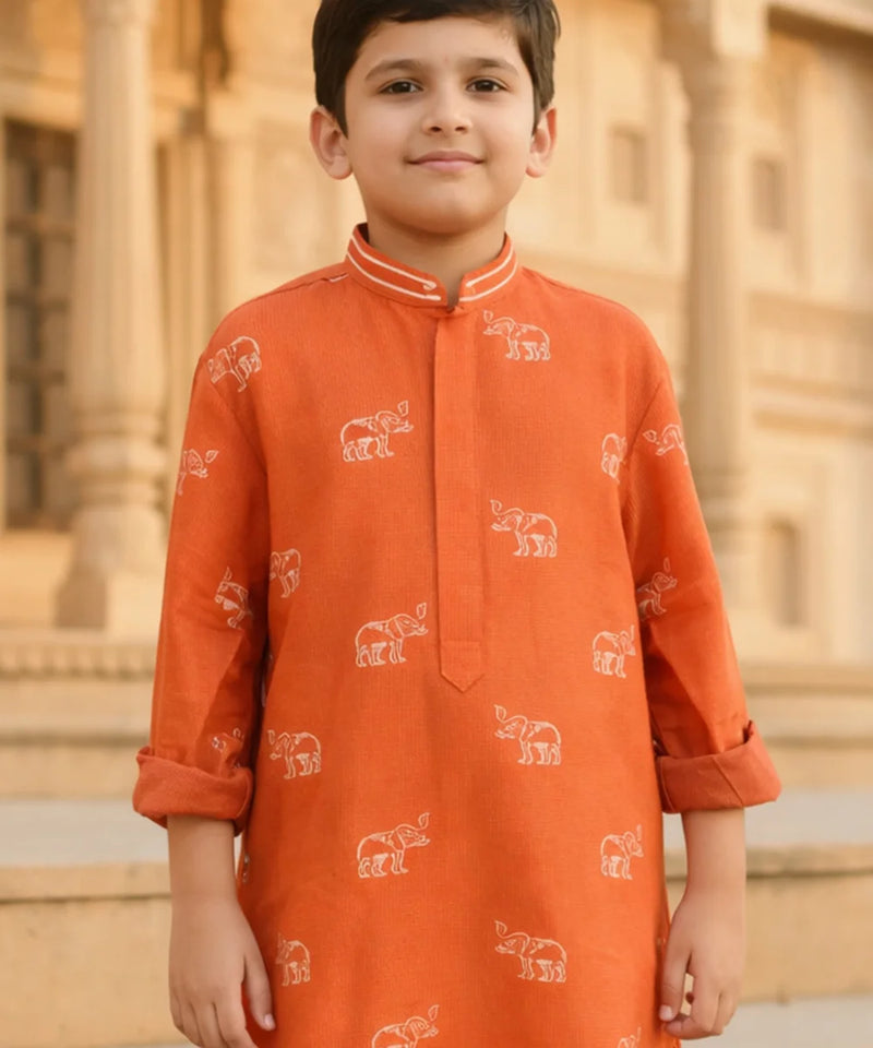 Child wearing an orange kurta with elephant patterns in front of a building.
