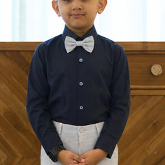 Young boy wearing a navy shirt with a white bow tie against a wooden background