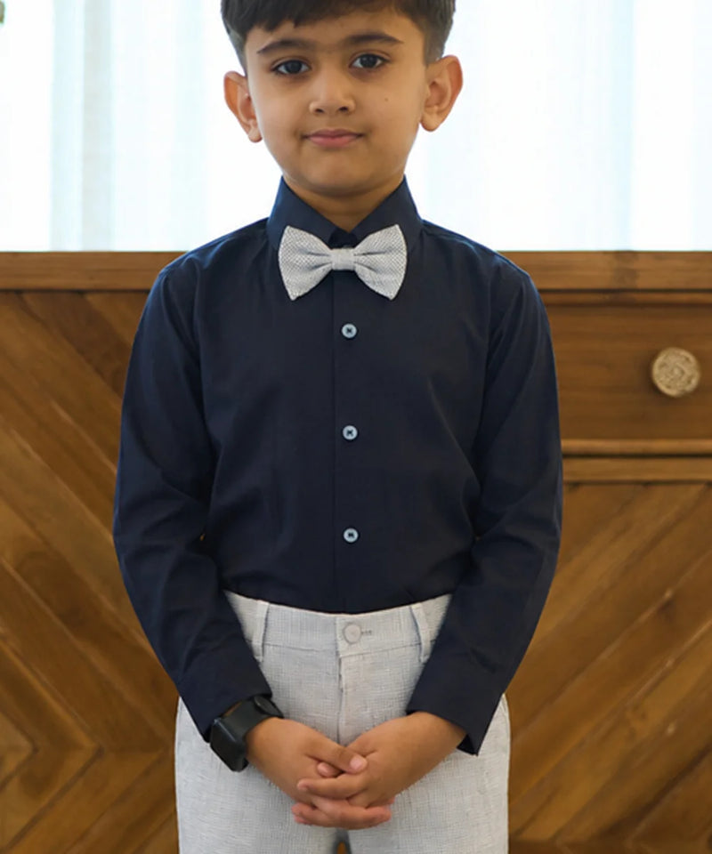 Young boy wearing a navy shirt with a white bow tie against a wooden background
