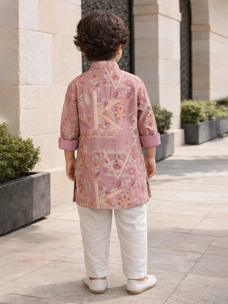 Child wearing a pink embroidered kurta with white pants standing outdoors.