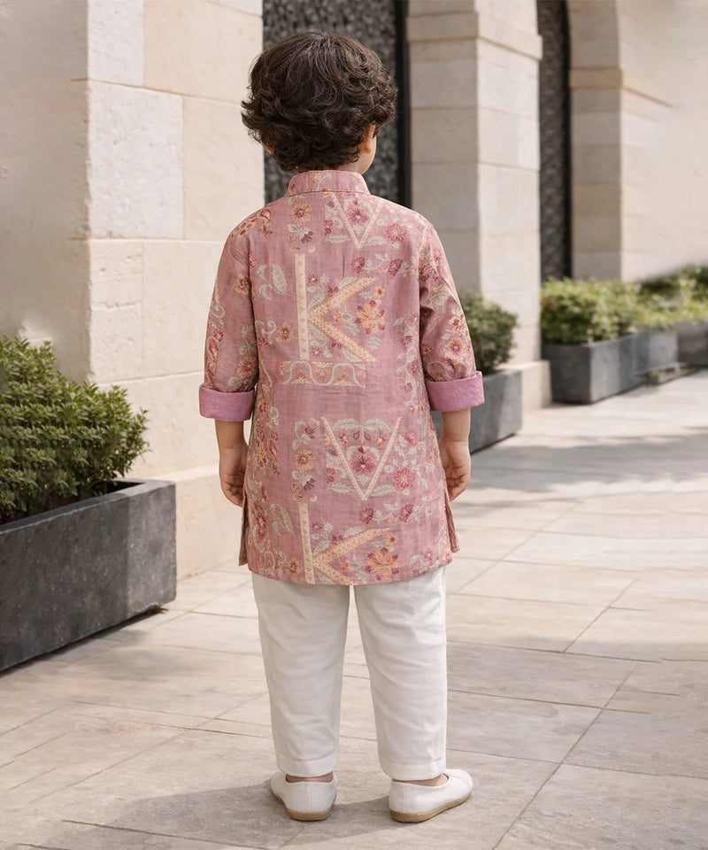 Child wearing a pink embroidered kurta with white pants standing outdoors.