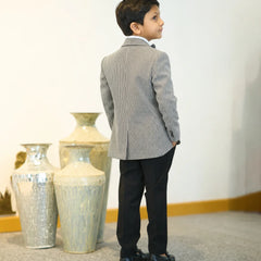 Young boy in a gray suit standing in front of decorative vases.
