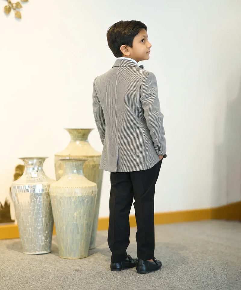 Young boy in a gray suit standing in front of decorative vases.