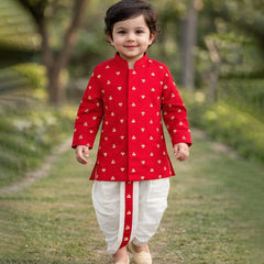 Child wearing a red traditional outfit with white patterns, standing outdoors on a grassy path.