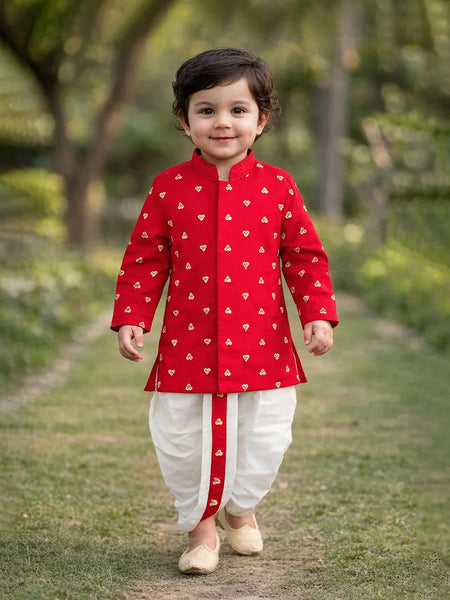 Child wearing a red traditional outfit with white patterns, standing outdoors on a grassy path.