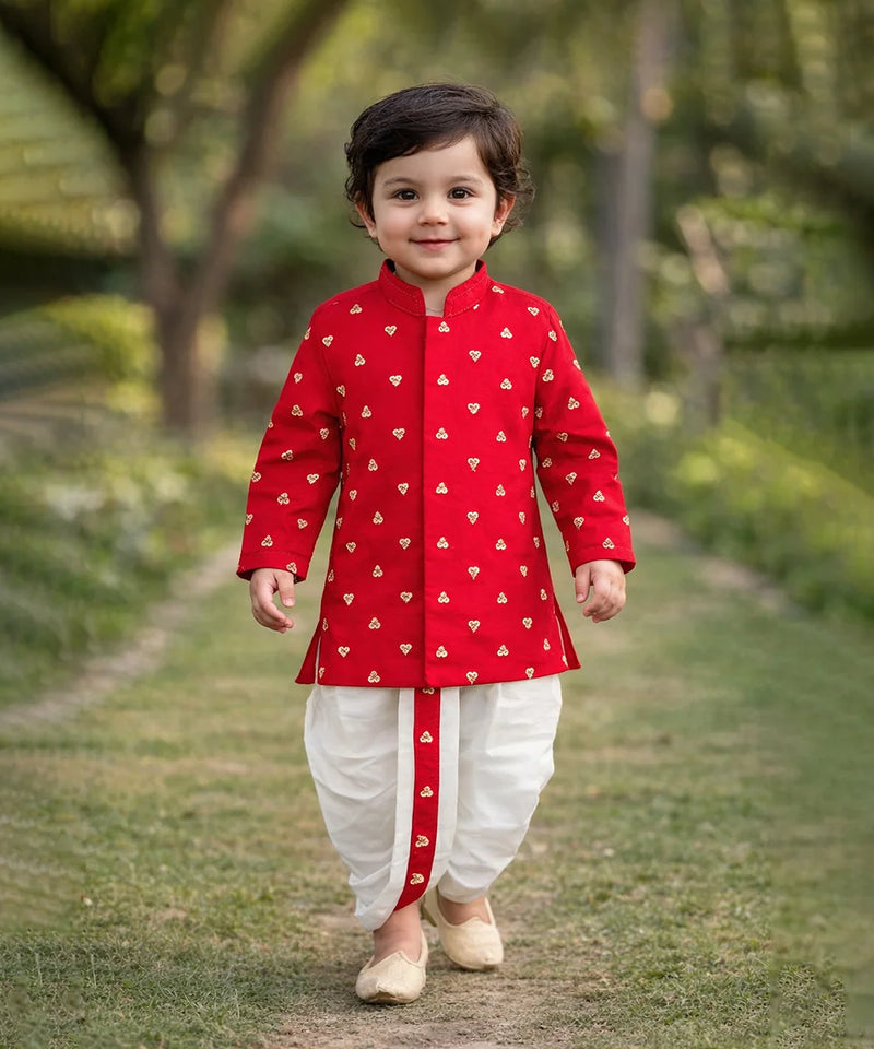 Child wearing a red traditional outfit with white patterns, standing outdoors on a grassy path.