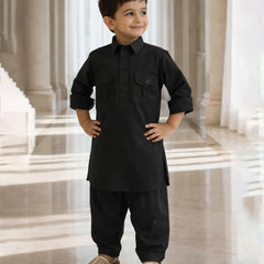 Young boy in a black traditional outfit standing in a bright, elegant interior setting.