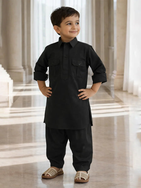 Young boy in a black traditional outfit standing in a bright, elegant interior setting.