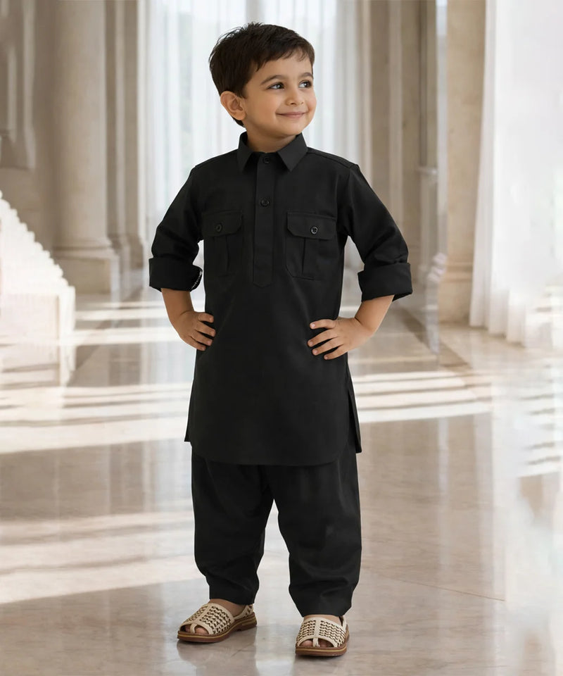 Young boy in a black traditional outfit standing in a bright, elegant interior setting.