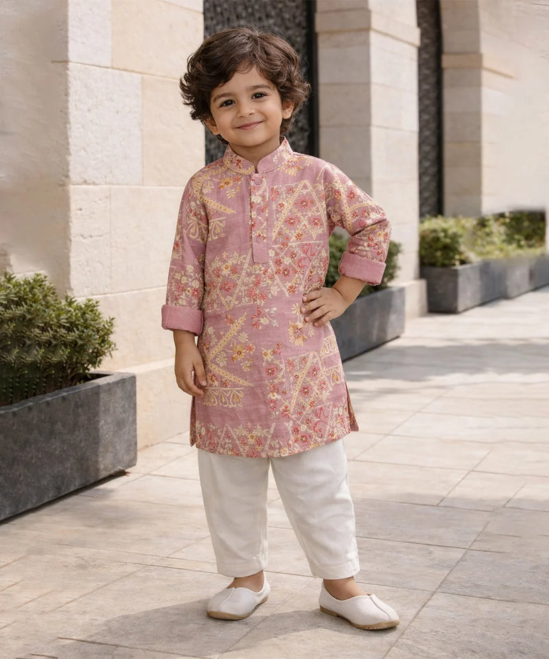 Child wearing a pink floral kurta with white pants standing outdoors.