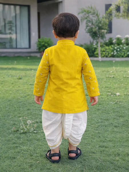 Child wearing a yellow kurta with white dhoti standing on grass