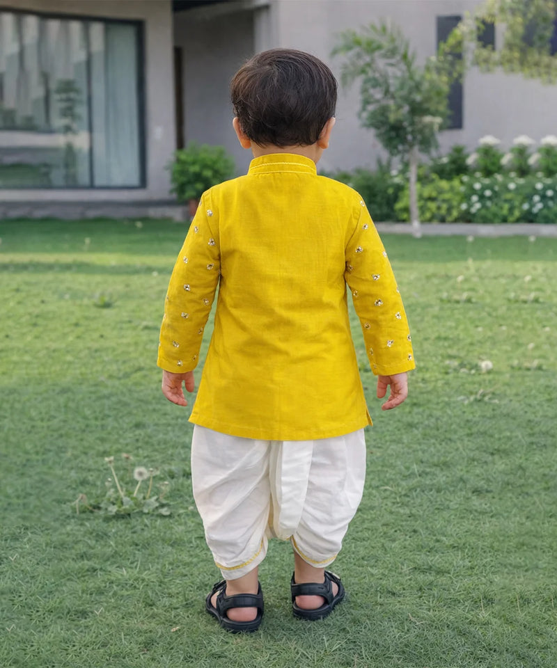 Child wearing a yellow kurta with white dhoti standing on grass
