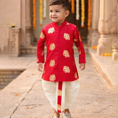 Child wearing a red kurta with gold patterns in an outdoor setting