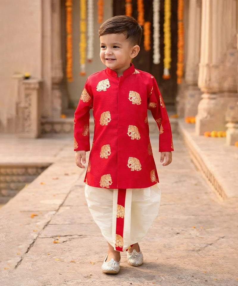 Child wearing a red kurta with gold patterns in an outdoor setting