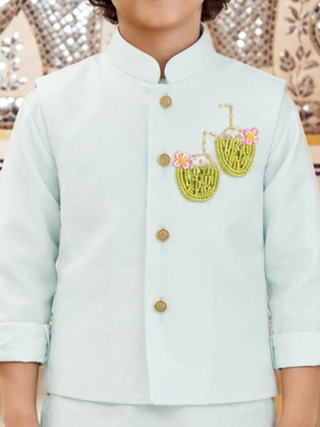 A child wearing a light mint green traditional Indian jacket with gold buttons and embroidered coconut motifs on the chest, paired with matching trousers.