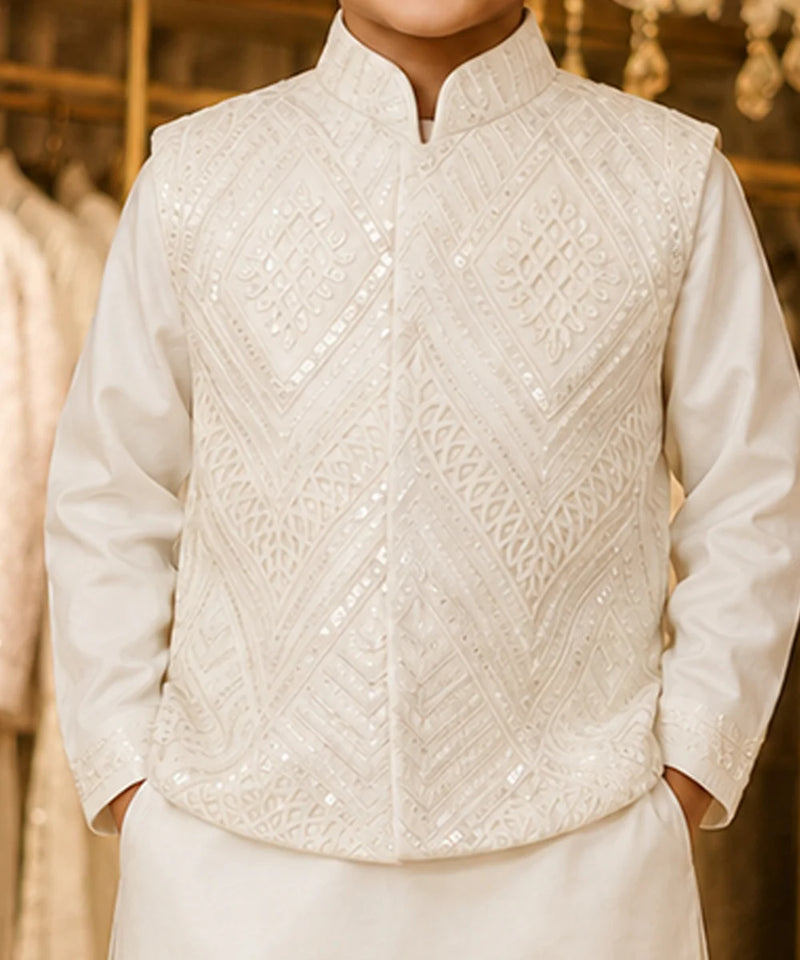 A close-up of a person wearing a white embroidered traditional jacket over a white long-sleeve shirt, with a softly blurred warm-toned indoor background.