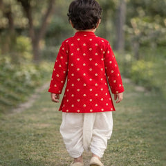 Child wearing a red traditional outfit with white patterns, walking on a grassy path.