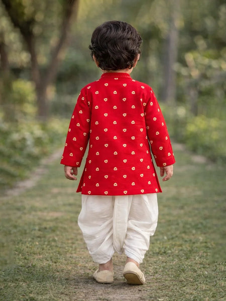 Child wearing a red traditional outfit with white patterns, walking on a grassy path.