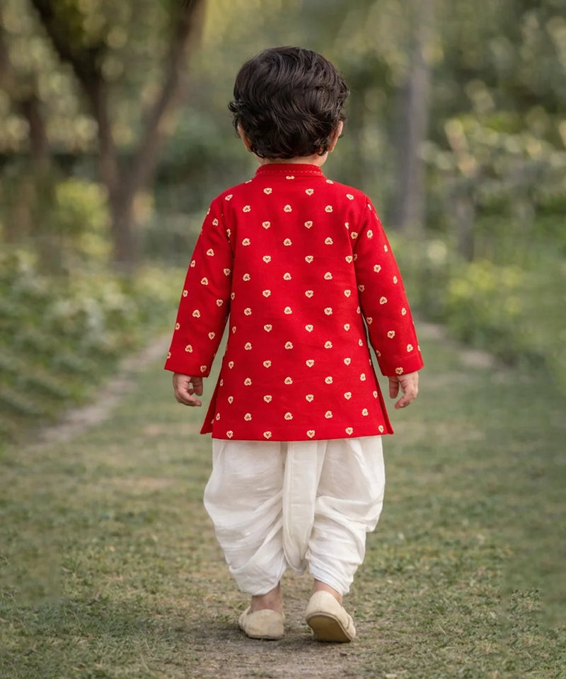 Child wearing a red traditional outfit with white patterns, walking on a grassy path.