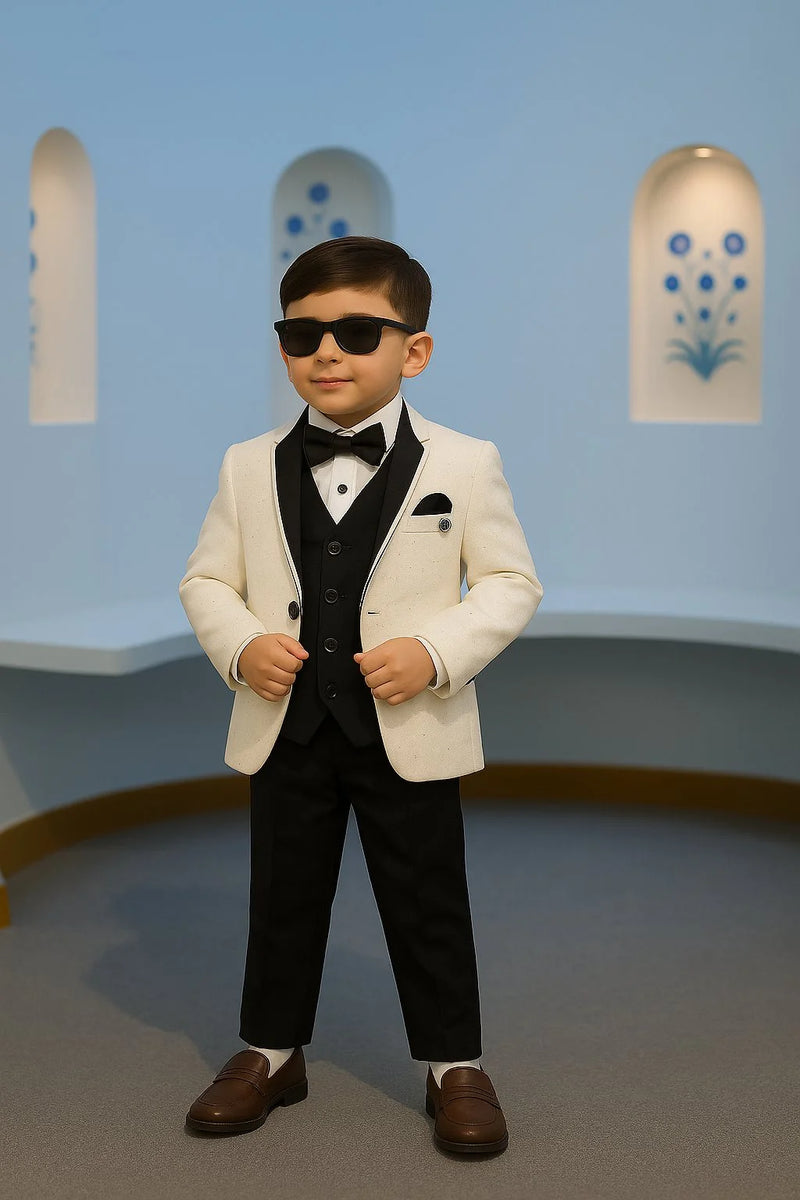 Young boy in a formal suit with sunglasses standing against a light blue wall.