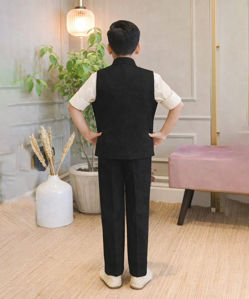 Person wearing a black vest and pants in a room with plants and a pink stool.