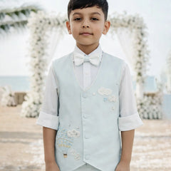 Young boy in formal attire with a light blue vest and white shirt against a decorative background.