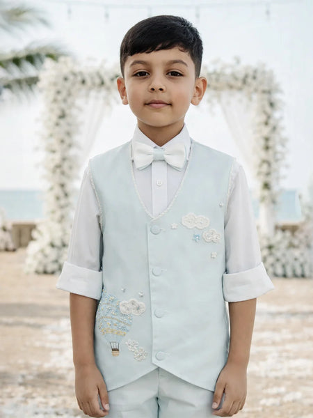 Young boy in formal attire with a light blue vest and white shirt against a decorative background.