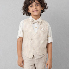 Young boy wearing a beige checkered vest, white shirt, and bow tie against a gray background