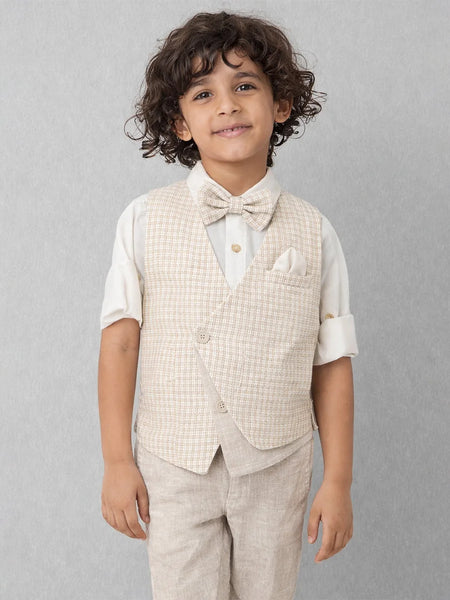 Young boy wearing a beige checkered vest, white shirt, and bow tie against a gray background