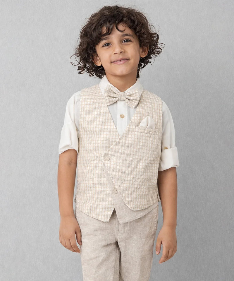 Young boy wearing a beige checkered vest, white shirt, and bow tie against a gray background