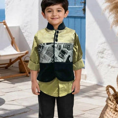 A young boy stands outdoors wearing a two-piece outfit consisting of a sage green and black jacket with a newspaper graphic print, paired with black trousers and cream sneakers.