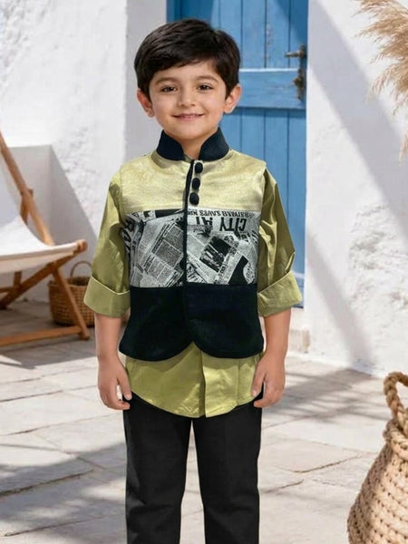 A young boy stands outdoors wearing a two-piece outfit consisting of a sage green and black jacket with a newspaper graphic print, paired with black trousers and cream sneakers.