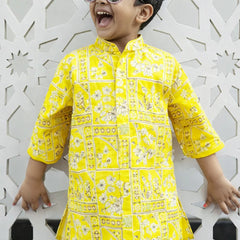 Child wearing a yellow patterned shirt against a decorative white wall.