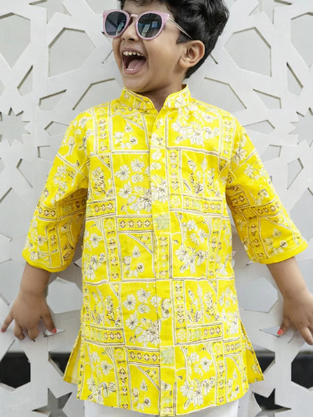 Child wearing a yellow patterned shirt against a decorative white wall.