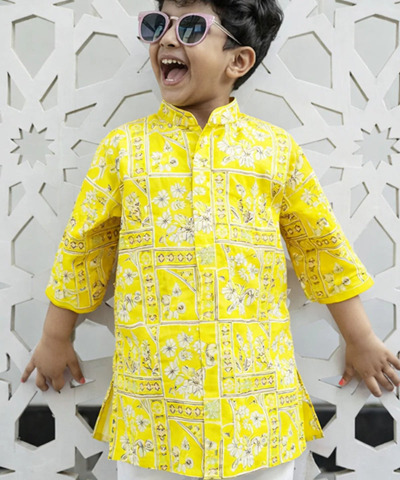 Child wearing a yellow patterned shirt against a decorative white wall.