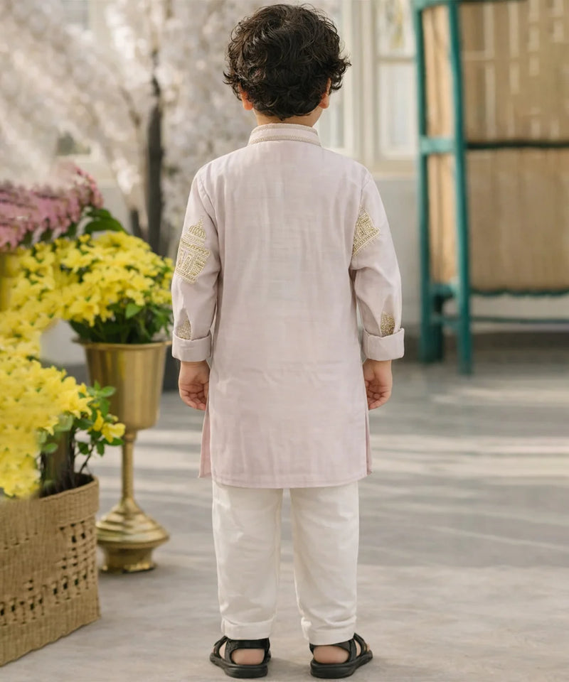 Child wearing a traditional outfit standing in a decorative setting with flowers and a green door.