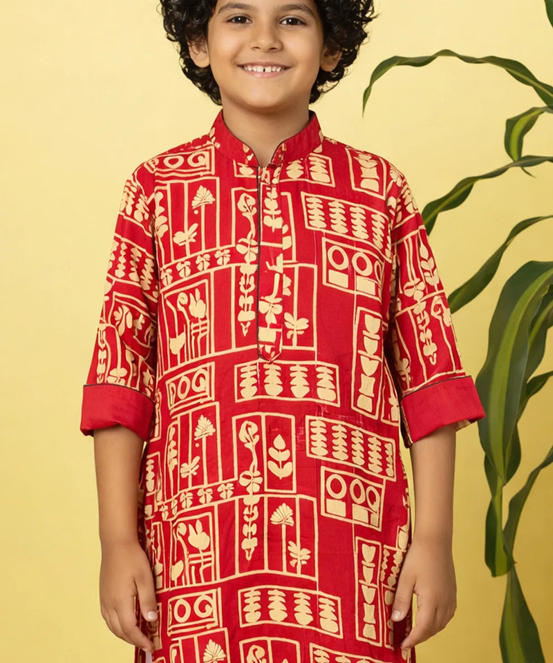 Child wearing a red traditional kurta with white patterns on a yellow background