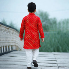 Person wearing a red kurta with white pants walking on a wooden bridge.