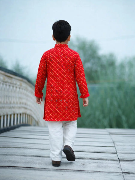 Person wearing a red kurta with white pants walking on a wooden bridge.