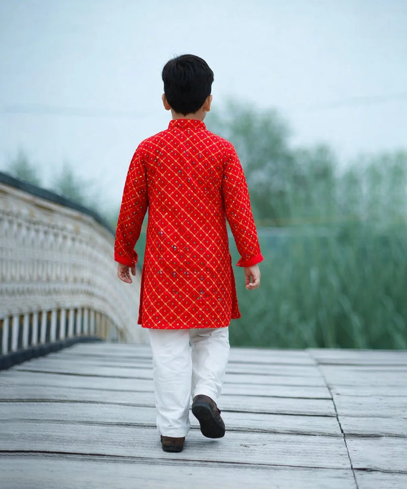 Person wearing a red kurta with white pants walking on a wooden bridge.