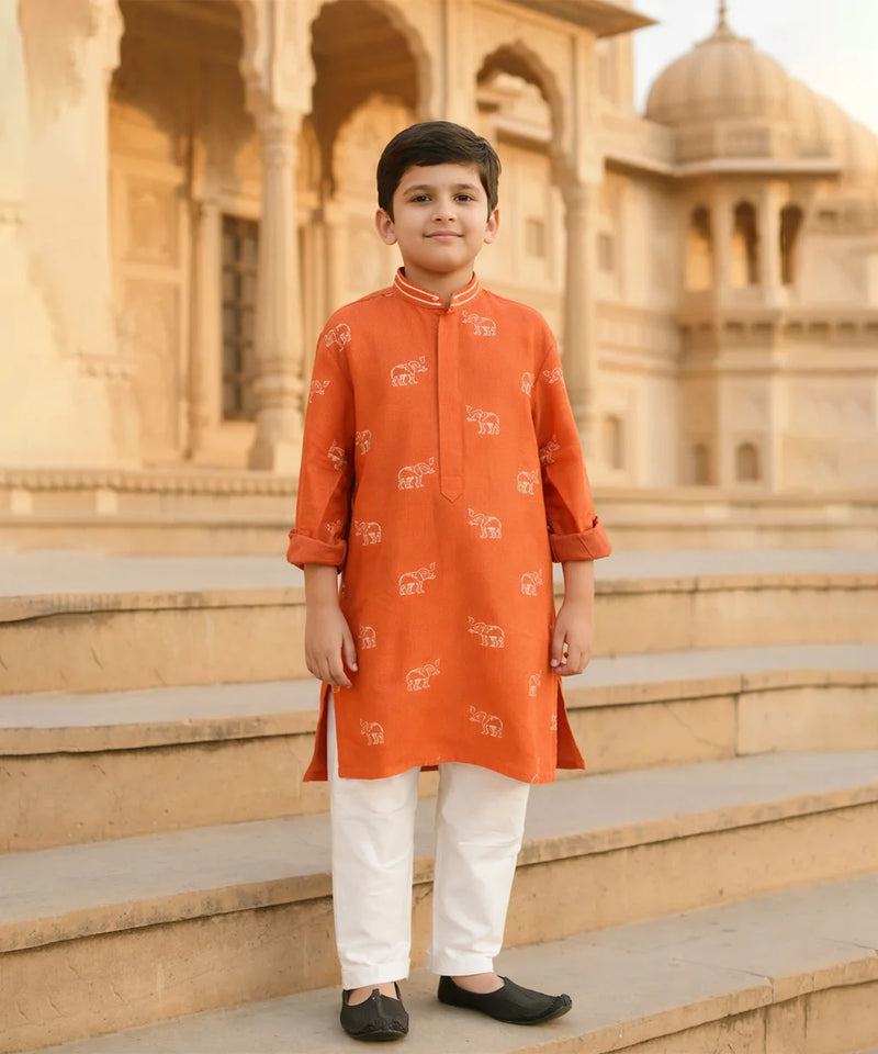 Child wearing an orange kurta with white patterns standing on steps in front of a historic building.
