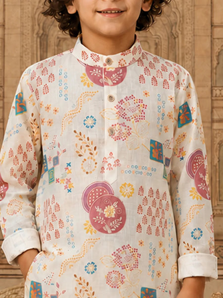 A child wearing a long-sleeve kurta with a white base and colorful traditional Indian print motifs, set against a warm, ornate architectural background.